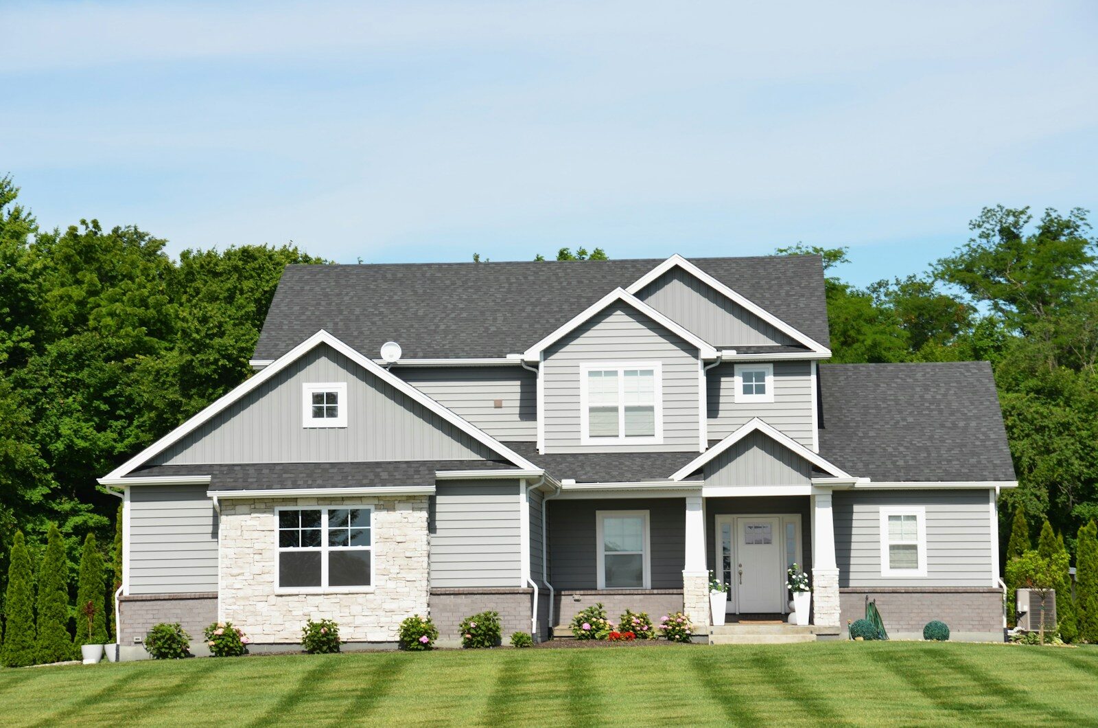 A modern grey house with a green lawn and trees.